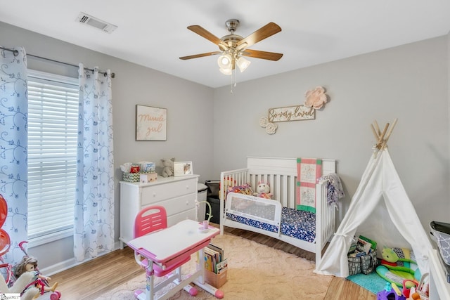 bedroom featuring ceiling fan, a crib, and light wood-type flooring