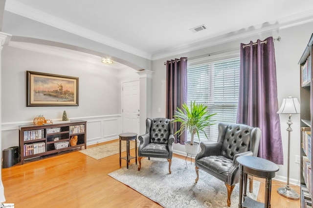 living area with ornate columns, crown molding, and wood-type flooring