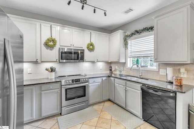 kitchen featuring dark stone counters, track lighting, sink, light tile patterned floors, and stainless steel appliances