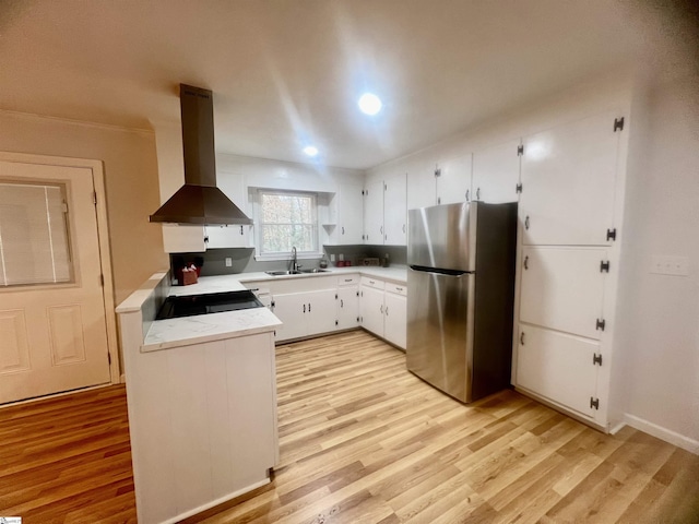 kitchen featuring stainless steel refrigerator, white cabinetry, sink, wall chimney exhaust hood, and light hardwood / wood-style floors