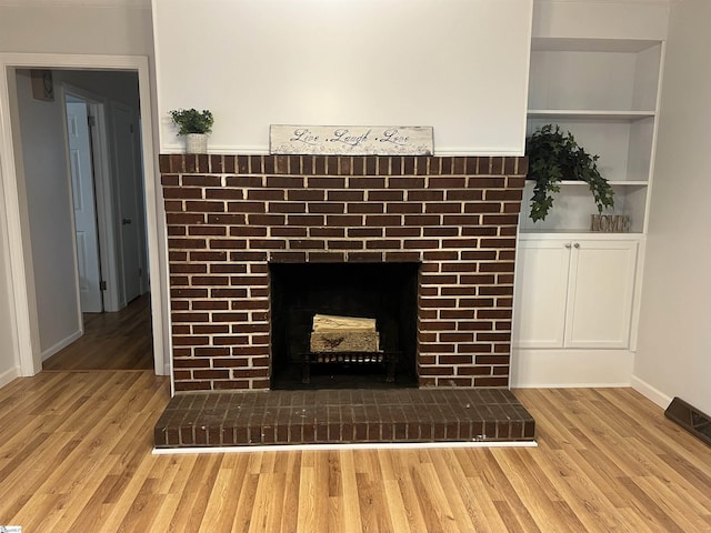 interior details featuring built in shelves, hardwood / wood-style flooring, and a brick fireplace