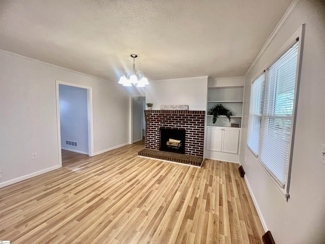 unfurnished living room with a brick fireplace, ornamental molding, built in shelves, light hardwood / wood-style flooring, and a notable chandelier