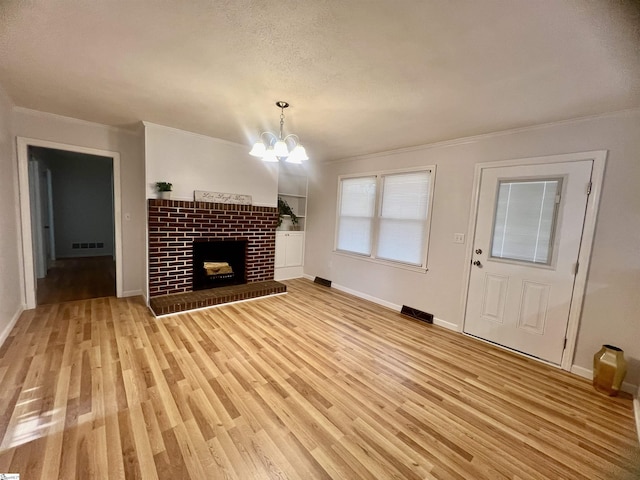 unfurnished living room featuring ornamental molding, built in shelves, a notable chandelier, a fireplace, and light hardwood / wood-style floors