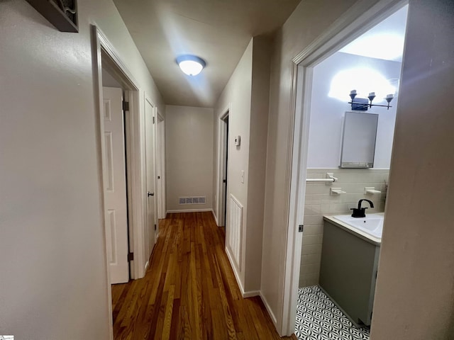 hall with sink, dark wood-type flooring, and tile walls