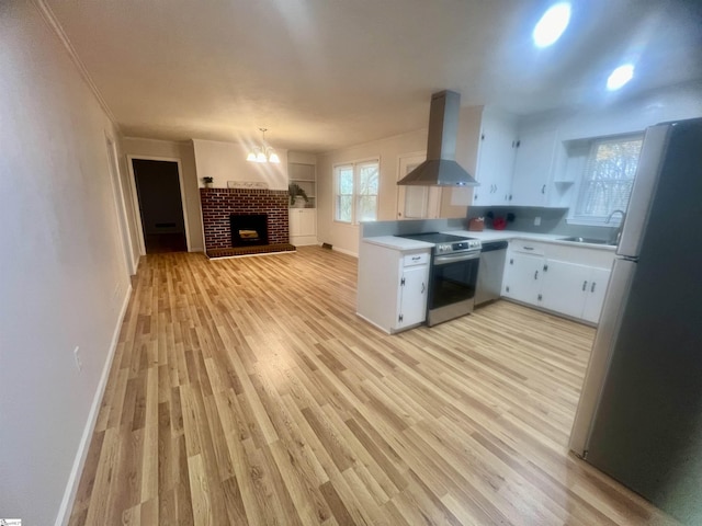 kitchen featuring appliances with stainless steel finishes, a brick fireplace, wall chimney range hood, light hardwood / wood-style flooring, and white cabinetry