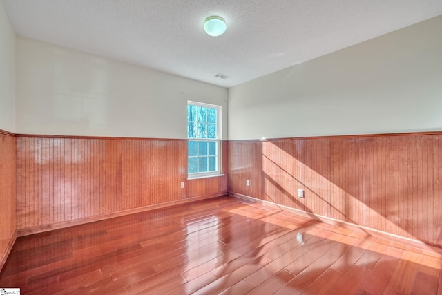 spare room featuring wooden walls, a textured ceiling, and hardwood / wood-style flooring