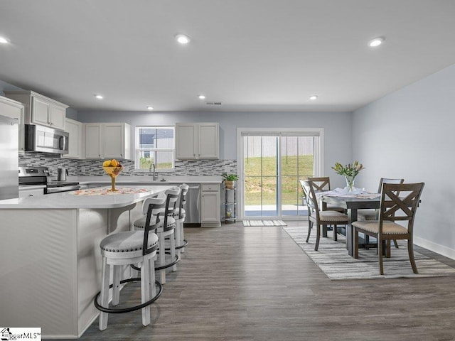 kitchen with a kitchen breakfast bar, decorative backsplash, dark wood-type flooring, and appliances with stainless steel finishes