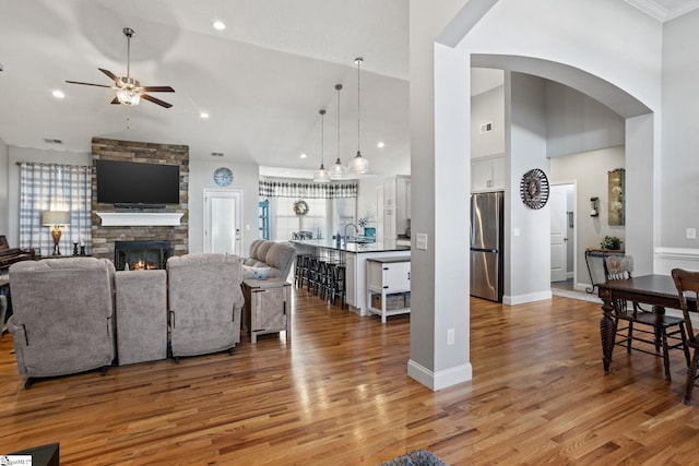 living room featuring ceiling fan, light hardwood / wood-style floors, a stone fireplace, and high vaulted ceiling