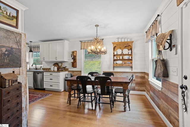 dining space with a notable chandelier, plenty of natural light, light wood-type flooring, and wooden walls