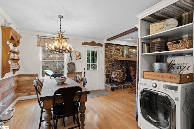 dining space featuring wood walls, crown molding, light hardwood / wood-style flooring, a notable chandelier, and washer / dryer