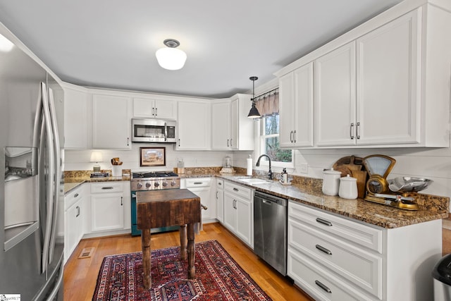 kitchen with sink, stainless steel appliances, dark stone countertops, pendant lighting, and white cabinets