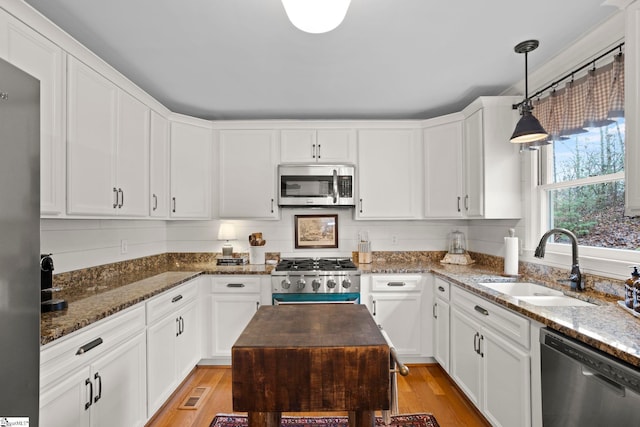 kitchen with white cabinets, sink, stainless steel appliances, and hanging light fixtures