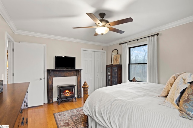 bedroom with a wood stove, crown molding, light hardwood / wood-style flooring, ceiling fan, and a closet