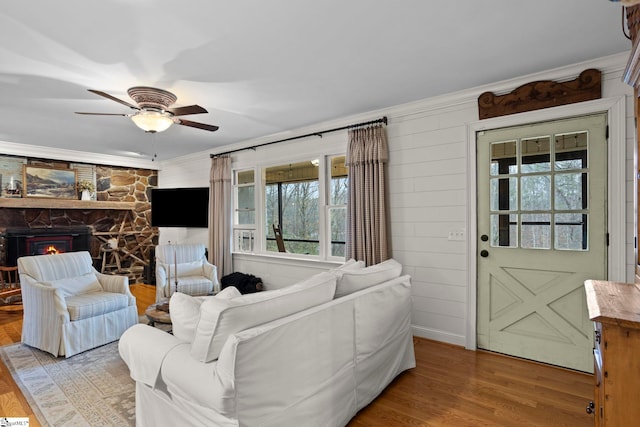 living room featuring hardwood / wood-style flooring, a stone fireplace, ceiling fan, and crown molding