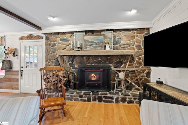 living room with wood-type flooring, a stone fireplace, ornamental molding, and beam ceiling