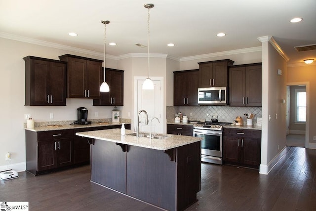 kitchen featuring stainless steel appliances, sink, decorative light fixtures, a breakfast bar area, and an island with sink