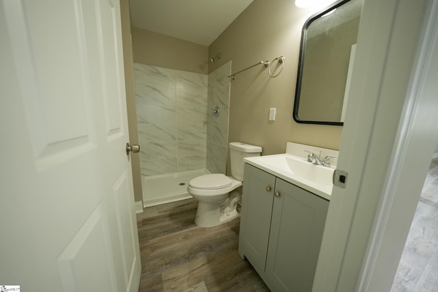 bathroom with tiled shower, hardwood / wood-style floors, vanity, and toilet