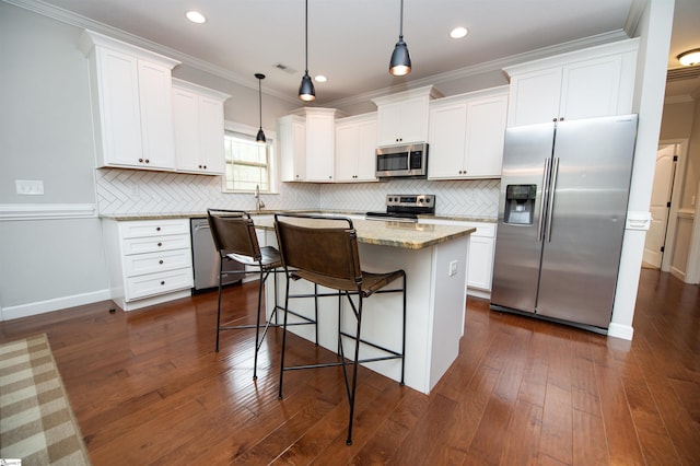 kitchen with appliances with stainless steel finishes, a kitchen island, pendant lighting, white cabinetry, and a breakfast bar area