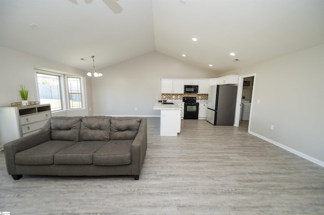 living room featuring sink, washer / dryer, light hardwood / wood-style floors, a chandelier, and vaulted ceiling