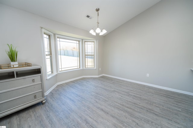 spare room with hardwood / wood-style floors, vaulted ceiling, and a notable chandelier