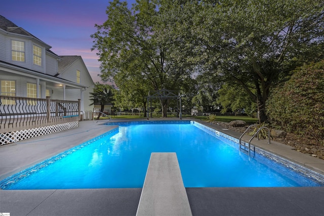 pool at dusk featuring a diving board