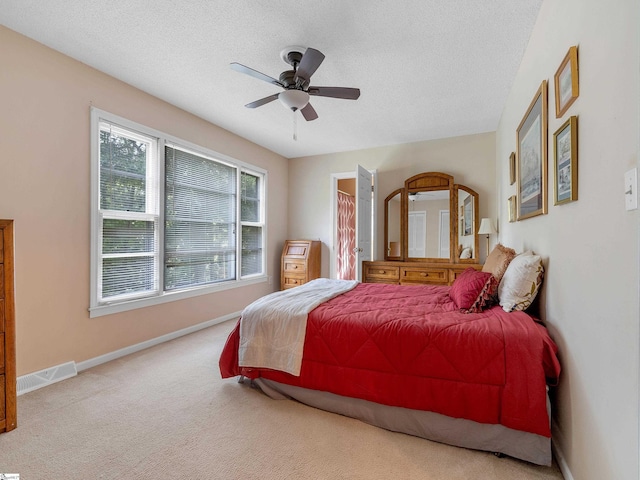 bedroom with ceiling fan, light colored carpet, and a textured ceiling