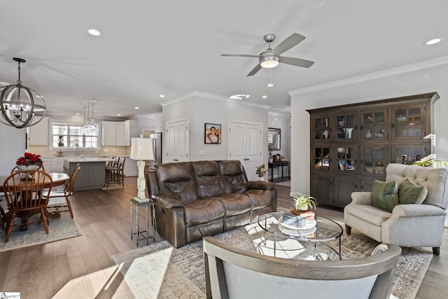 living room featuring ceiling fan with notable chandelier, light hardwood / wood-style floors, ornamental molding, and sink