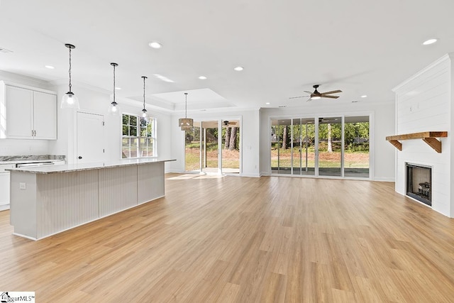 unfurnished living room with light wood-type flooring, a raised ceiling, ceiling fan, and crown molding