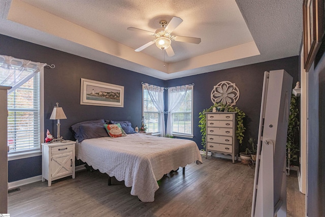 bedroom featuring hardwood / wood-style floors, ceiling fan, multiple windows, and a tray ceiling