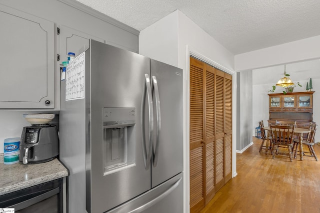 kitchen with stainless steel fridge, light hardwood / wood-style flooring, light stone counters, and a textured ceiling