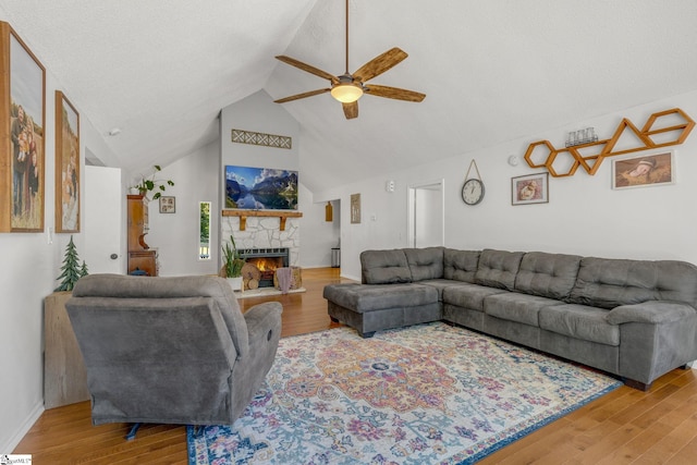 living room with hardwood / wood-style flooring, ceiling fan, a stone fireplace, and high vaulted ceiling