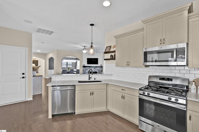 kitchen with sink, dark hardwood / wood-style flooring, kitchen peninsula, cream cabinets, and appliances with stainless steel finishes