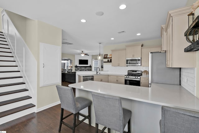 kitchen featuring a kitchen breakfast bar, hanging light fixtures, ceiling fan, appliances with stainless steel finishes, and kitchen peninsula