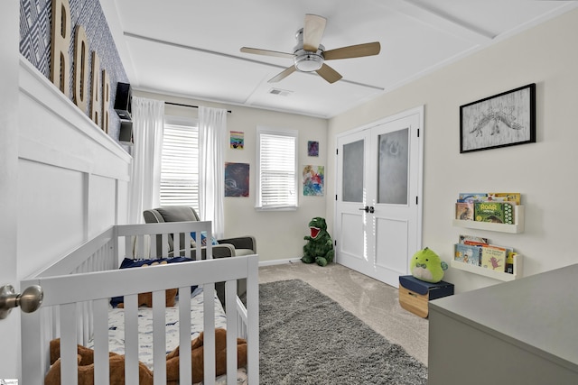 carpeted bedroom featuring a nursery area and ceiling fan