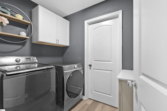 clothes washing area featuring cabinets, light hardwood / wood-style floors, and washer and clothes dryer