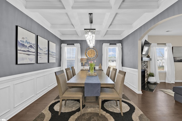 dining room featuring dark wood-type flooring, coffered ceiling, a stone fireplace, a notable chandelier, and beam ceiling