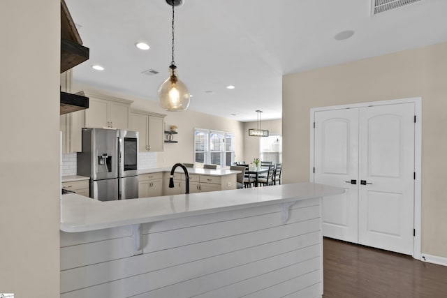 kitchen featuring tasteful backsplash, kitchen peninsula, stainless steel fridge, pendant lighting, and a breakfast bar area