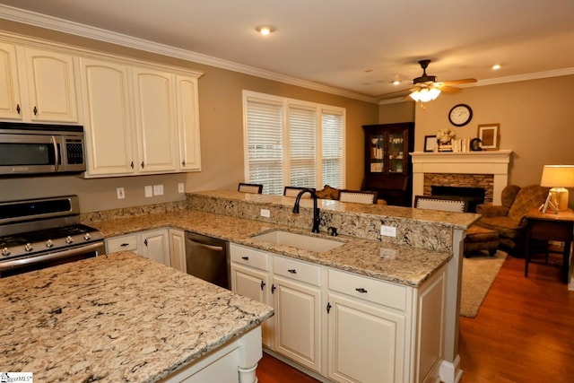 kitchen with sink, ceiling fan, a fireplace, kitchen peninsula, and stainless steel appliances