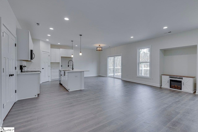 kitchen with wood finished floors, open floor plan, light countertops, stainless steel microwave, and a glass covered fireplace