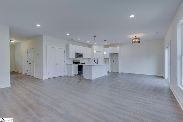 unfurnished living room with light wood-type flooring, baseboards, a sink, and recessed lighting