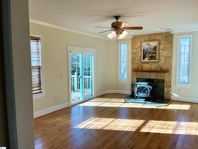 unfurnished living room with ceiling fan, light hardwood / wood-style floors, a wood stove, and crown molding