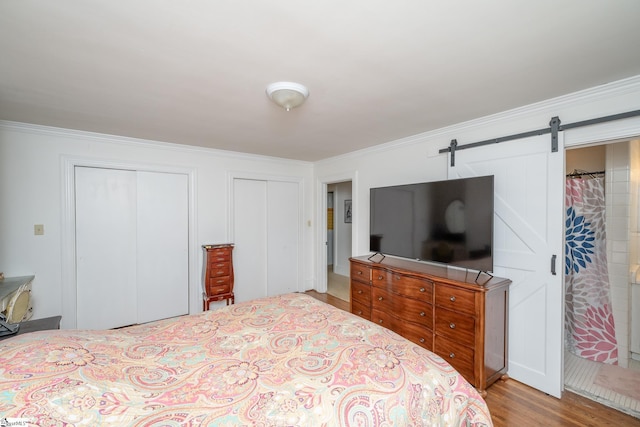 bedroom featuring a barn door, crown molding, light hardwood / wood-style flooring, and multiple closets