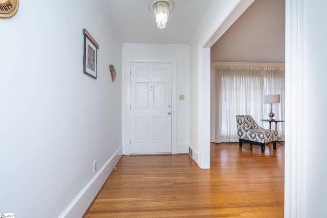 foyer entrance featuring light wood-type flooring, ornamental molding, and a chandelier