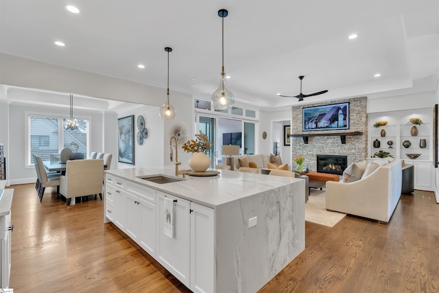 kitchen with light stone countertops, a raised ceiling, sink, pendant lighting, and a center island with sink