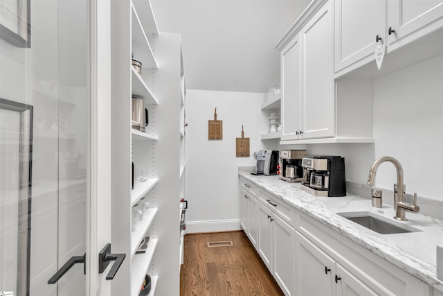 kitchen with white cabinets, dark hardwood / wood-style flooring, light stone counters, and sink