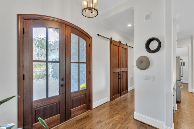 foyer entrance featuring french doors, a barn door, light hardwood / wood-style flooring, a chandelier, and ornamental molding