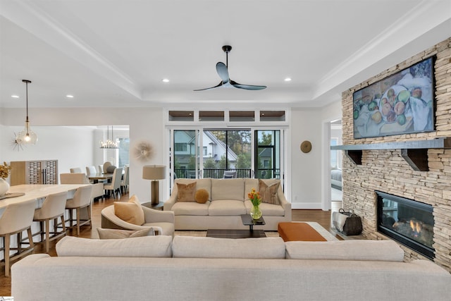 living room with a raised ceiling, a stone fireplace, ceiling fan, and hardwood / wood-style flooring