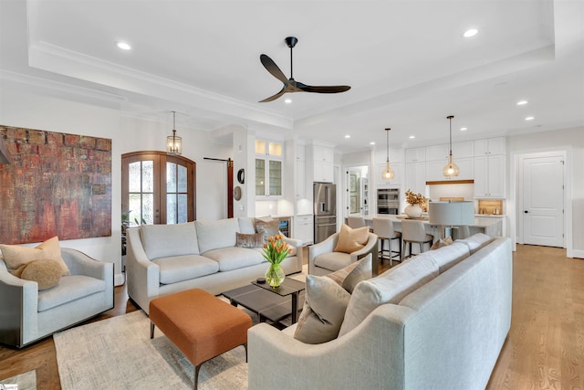 living room featuring french doors, light wood-type flooring, ornamental molding, a raised ceiling, and ceiling fan