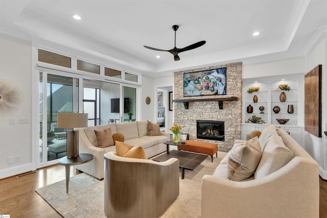 living room featuring ceiling fan, light hardwood / wood-style floors, a fireplace, and a tray ceiling