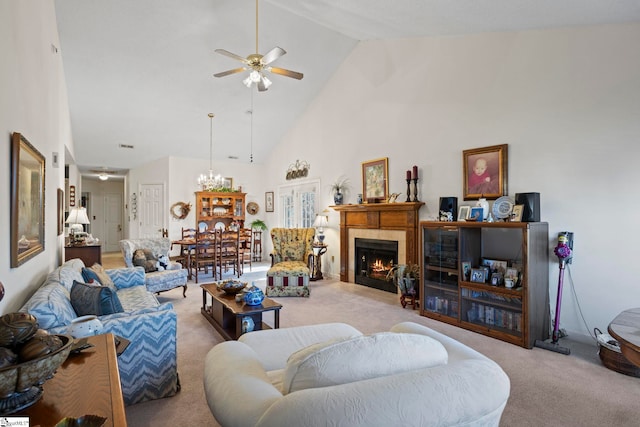 carpeted living room featuring a tiled fireplace, high vaulted ceiling, and ceiling fan with notable chandelier